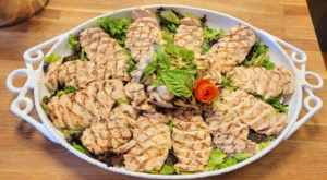 Grilled chicken slices served on a large platter with fresh lettuce, herbs and vegetable garnish for halal catering