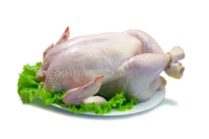 Whole raw chicken displayed on a white plate with fresh lettuce